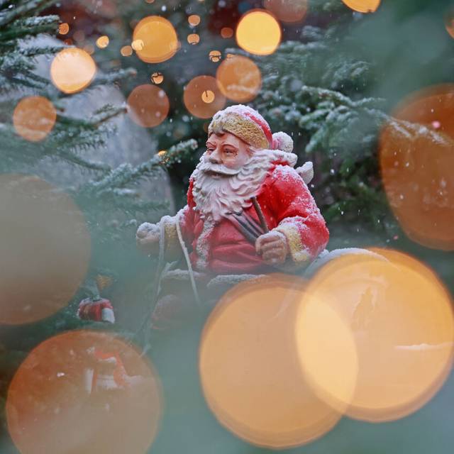 Blick durch eine Lichterkette auf eine schneebedeckte Weihnachtsmannfigur