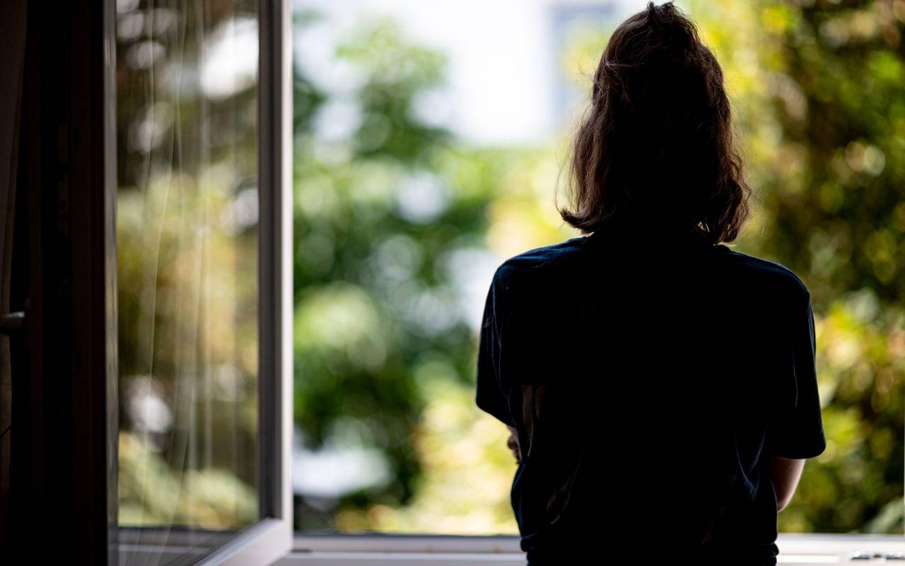 Eine junge Frau steht in ihrer Wohnung an einem Fenster