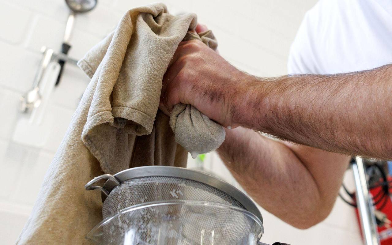 Ein Mann trennt Proteine von erhitzter Milch mit einem Käsetuch