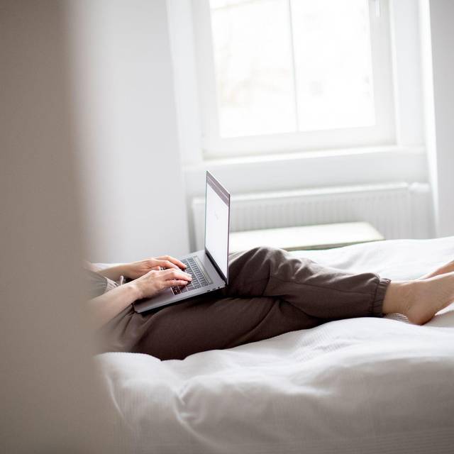 Eine Frau sitzt mit Laptop auf einem Bett