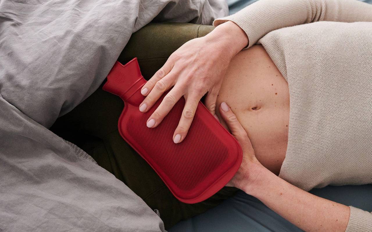 Frau hält sich eine Wärmflasche an den Unterbauch