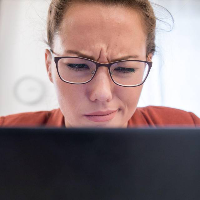 Eine junge Frau blickt skeptisch auf ihren Laptop