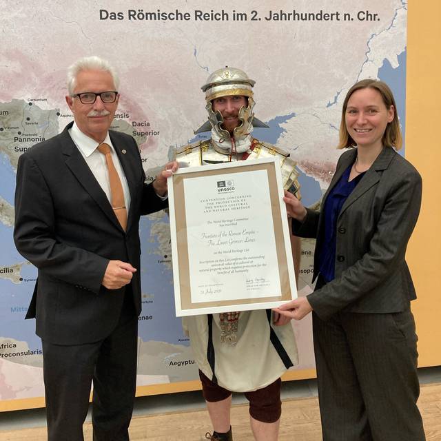 Landrat Thomas Hendele und Estelle Dageroth, Wirtschaftsförderung der Stadt Monheim am Rhein mit römischer Unterstützung halten die offizielle Urkunde in Händen. 