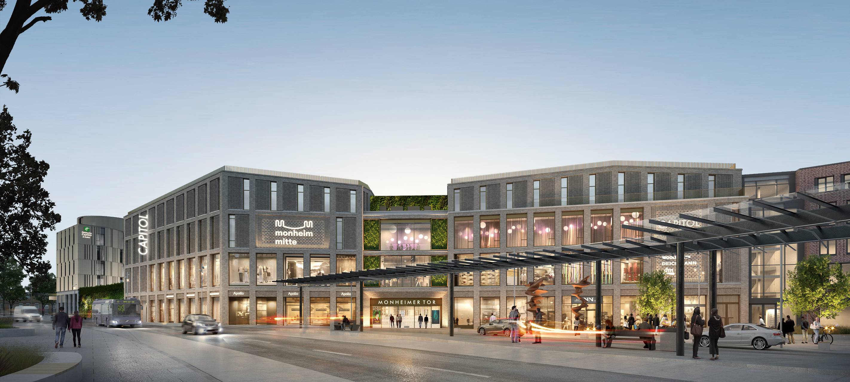 Blick über den Monheimer Busbahnhof auf das künftige neue Monheimer Tor. Mittig über dem Eingang und rechts davon, im zweiten und dritten Stock, ist das hell erleuchtete Kino-Foyer zu erkennen, unten davor die Tanzenden Säulen von Tony Cragg. Im Erdgeschoss das Textilangebot von Sinn. Hinten links das neue Holiday Inn Express Hotel