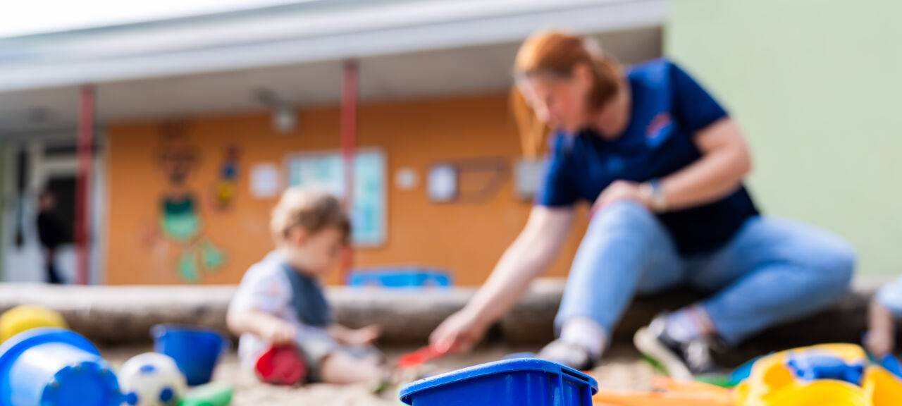 Ein Kind spielt mit einer Erzieherin im Sandkasten einer Kita.