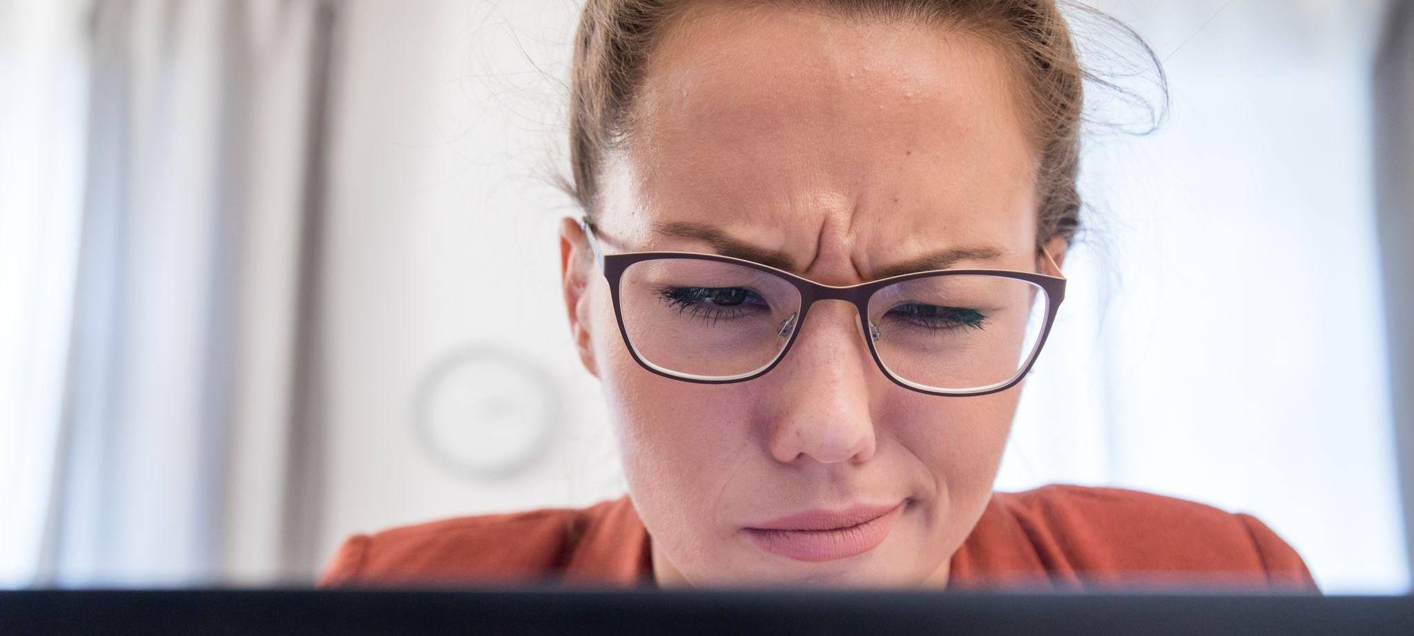 Eine junge Frau blickt skeptisch auf ihren Laptop
