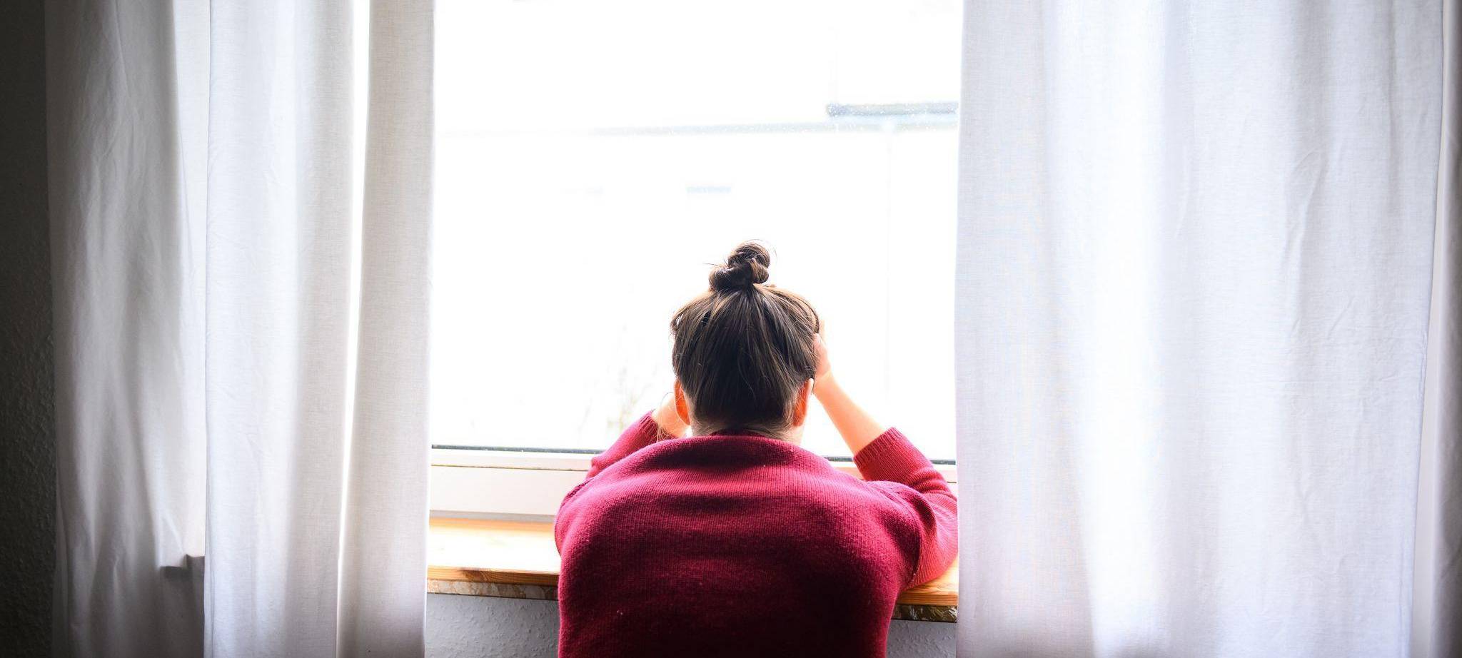 Frau sitzt mit Kopf in den Händen am Fenster