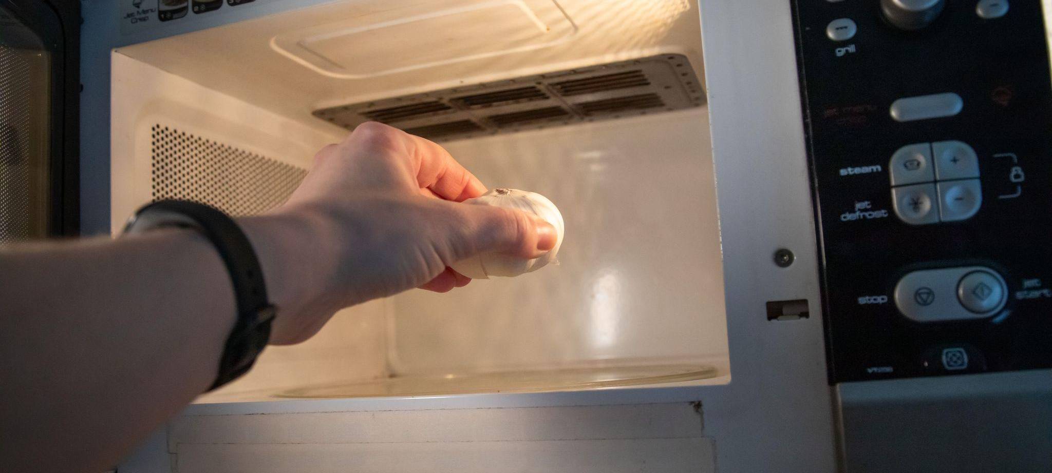 Eine Frau legt eine Knoblauchknolle in die Mikrowelle